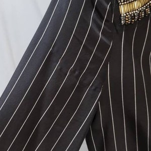 Pode incluir: Camisa de manga comprida listrada em preto e branco com um enfeite de contas no ombro.