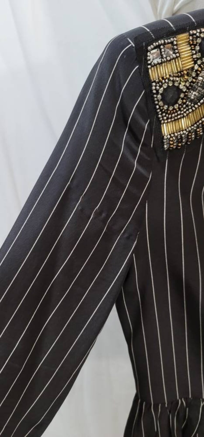 Pode incluir: Camisa de manga comprida listrada em preto e branco com um enfeite de contas no ombro.