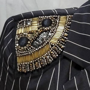 Pode incluir: Uma camisa listrada em preto e branco com um enfeite de contas douradas e prateadas no ombro.
