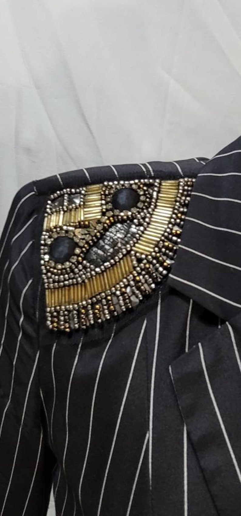 Pode incluir: Uma camisa listrada em preto e branco com um enfeite de contas douradas e prateadas no ombro.