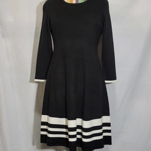 May include: Black sweater dress with white stripes at the hem. The dress has long sleeves and a round neckline.