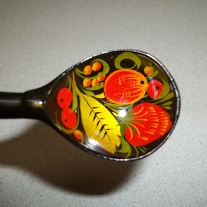 May include: A wooden spoon with a black handle and a painted design of red, yellow, and green flowers and leaves.