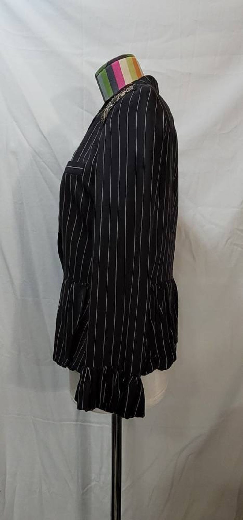 Pode incluir: Um blazer preto e branco listrado com uma bainha franjada. O blazer tem uma silhueta ajustada e um decote sem colarinho.