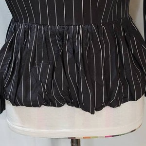 Pode incluir: Uma blusa listrada preta e branca com um babado franzido na parte inferior.