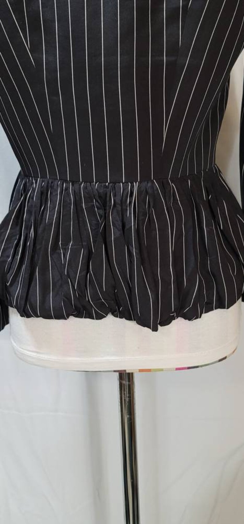 Pode incluir: Uma blusa listrada preta e branca com um babado franzido na parte inferior.