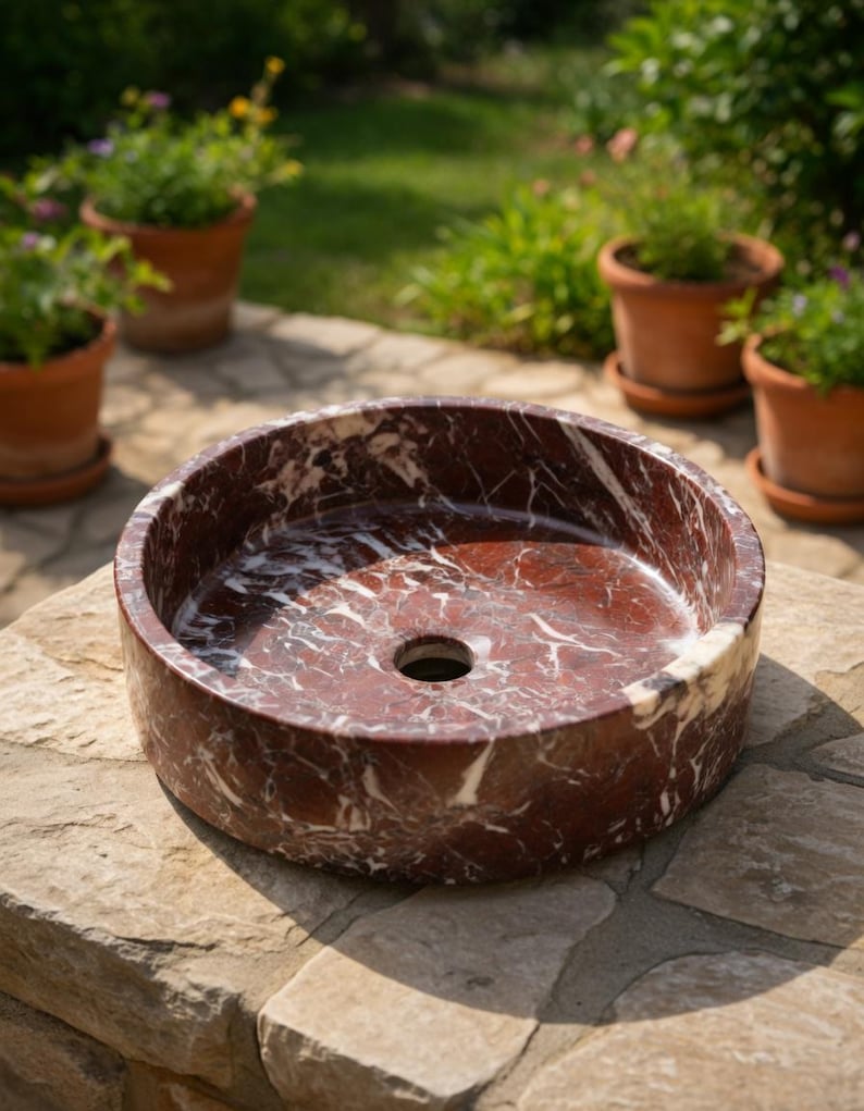 May include: A circular vessel sink crafted from deep red marble with prominent white veining throughout the stone. The basin features a smooth, polished finish and a centered circular drain hole, showcasing the natural patterns of the marble.