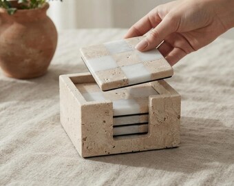 May include: A square stone coaster set featuring a checkerboard pattern of beige travertine and white marble squares. The set includes a matching square stone holder with a U-shaped cutout on the front, designed to store the stack of square coasters.