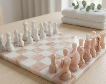 May include: A chess set featuring a board with alternating white and pink marble squares. The pieces are carved from matching white and pink stone, with one side in white and the other in pink, arranged in their starting positions on the board.