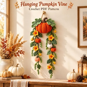 Op de afbeelding: Een gehaakte wandhanger met een grote oranje pompoen, kleinere pompoenen in oranje, wit en roze, groene bladeren en gele bloemen aan ranken. De tekst "Hanging Pumpkin Vine Crochet PDF Pattern" staat bovenaan de afbeelding.