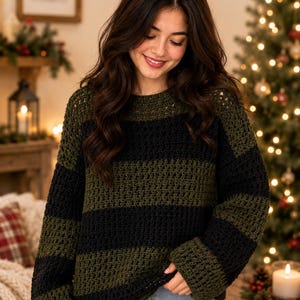 May include: A long-sleeved, crew-neck sweater featuring wide, horizontal stripes in alternating olive green and black. The garment is constructed with a visible, open-knit crochet stitch pattern, creating a textured appearance throughout the fabric.
