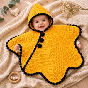May include: A bright yellow crocheted baby poncho with a pointed hood and a black scalloped border. The garment features three large black circular buttons down the front, creating a distinct contrast against the vibrant yellow yarn texture.