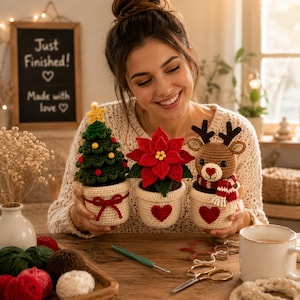 Puede incluir: Tres decoraciones de ganchillo en maceta que incluyen un árbol de Navidad verde con una estrella amarilla, una flor de pascua roja y un reno marrón con una bufanda roja y blanca. Cada pieza está en una maceta de ganchillo crema con detalles rojos.