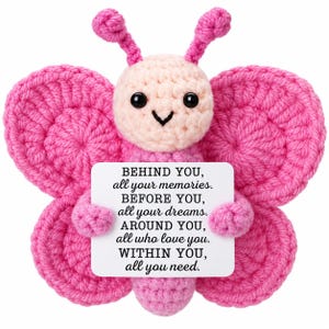 May include: A pink crocheted butterfly toy with a light pink head, black eyes, and two antennae, holding a white rectangular sign that reads: BEHIND YOU, all your memories. BEFORE YOU, all your dreams. AROUND YOU, all who love you. WITHIN YOU, all you need.