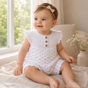 May include: A white crocheted romper featuring a round neckline, flutter sleeves, and three small brown buttons down the center chest. The garment is crafted with a textured, open-work stitch pattern throughout the bodice and leg openings.