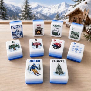 Peut inclure: Un ensemble de dix tuiles de mah-jong blanches à base bleue, chacune présentant des illustrations sur le thème de l'hiver et du texte, notamment SOAP, RED, GREEN, 9, E EAST, S SOUTH, 9, un flocon, JOKER avec un skieur et FLOWER avec un sapin.