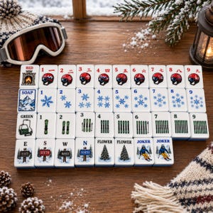 Peut inclure: Un ensemble de tuiles de mah-jong blanches ornées d'illustrations sur le thème de l'hiver, notamment des casques de ski, des flocons de neige, des skis, des sapins et des panneaux directionnels, disposées sur une surface en bois avec un bonnet.