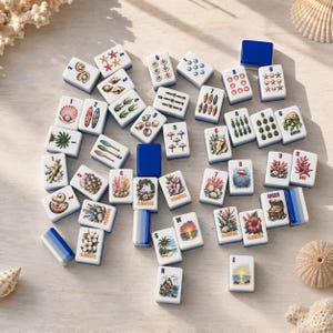 May include: A collection of rectangular mahjong tiles featuring various illustrations of seashells, tropical flowers, marine life, and beach scenes. Each white tile has blue edges and displays colourful graphics, with some tiles marked with numbers or text.