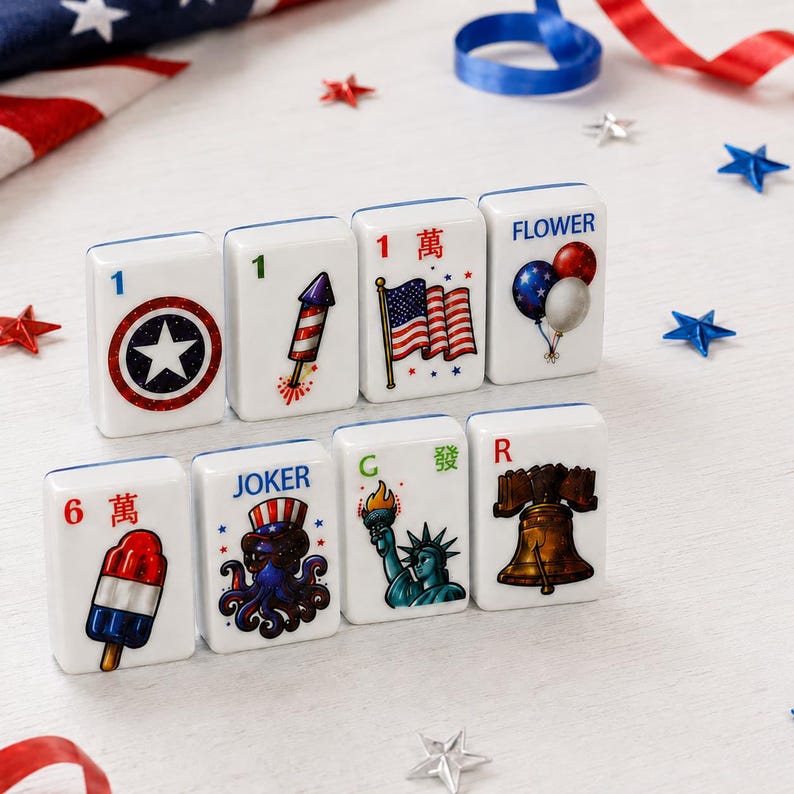 May include: A set of eight white rectangular mahjong tiles featuring patriotic American-themed illustrations. Designs include a star emblem, a firework, an American flag, balloons, a popsicle, an octopus wearing a hat, the Statue of Liberty, and a bell.