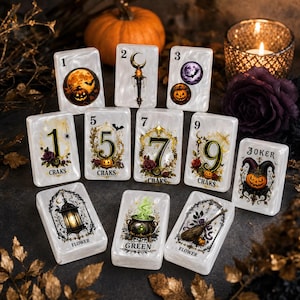 May include: A set of rectangular white tiles with pearlescent finish, featuring Halloween-themed illustrations including pumpkins, bats, a cauldron, a lantern, and a broom. Each tile displays numbers 1, 2, 3, 5, 7, 9, or the word Joker, Flower, or Green.