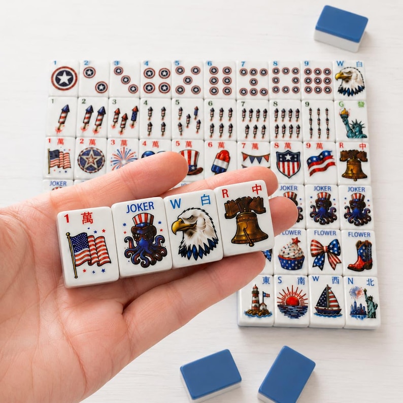 May include: A set of white mahjong tiles featuring patriotic American-themed illustrations including flags, eagles, fireworks, and the Liberty Bell. Four tiles are held in a row, displaying a flag, a joker octopus, an eagle, and a bell.