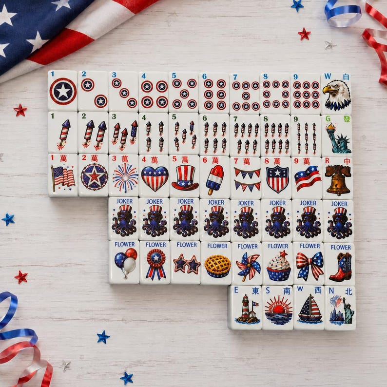 May include: A set of white mahjong tiles featuring patriotic American-themed illustrations including stars, fireworks, eagles, the Statue of Liberty, and various red, white, and blue icons. Each tile displays specific numbers, letters, or labels.