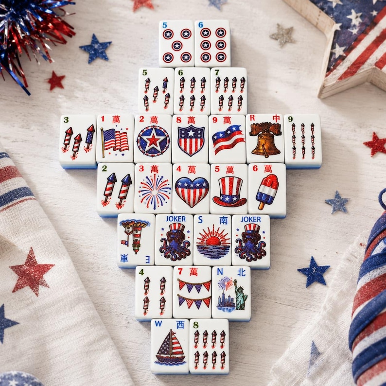 May include: A collection of white rectangular mahjong tiles arranged in a pyramid shape, featuring colorful patriotic American-themed illustrations including fireworks, flags, a liberty bell, a top hat, a sailboat, and the Statue of Liberty.