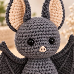 Handmade grey crochet bat amigurumi doll displayed on a wooden stand