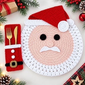 May include: A round crochet placemat shaped like a Santa Claus face with a red hat, white beard, black eyes, and a pink nose. Beside it is a rectangular red crochet cutlery holder featuring a white trim, two white buttons, and a black belt.