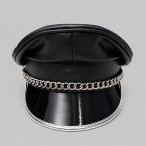 May include: A black leather military-style cap featuring a smooth, rounded crown and a structured, glossy black patent visor. A silver-toned metal chain is attached across the front, resting above the brim, which is finished with a silver trim.