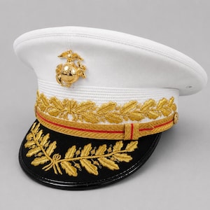May include: A white military-style peaked cap featuring a gold-colored Eagle, Globe, and Anchor emblem on the front. The band is decorated with gold oak leaf embroidery and a thin red stripe, while the black visor displays gold leaf detailing.