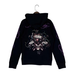 May include: A black hooded sweatshirt featuring a graphic on the back of a skull and heart with a banner that reads LOVE KILLS SLOWLY. The design includes purple vine accents and purple script text on the sleeves and near the hood neckline.