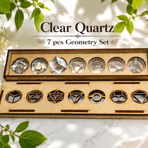 Könnte beinhalten: Ein Clear Quartz 7 pcs Geometry Set bestehend aus sieben facettierten klaren Quarzkristallen in einem Holztablett, begleitet von einem passenden Holzdeckel mit sieben kreisförmigen Ausschnitten für geometrische Drahtgitterformen.