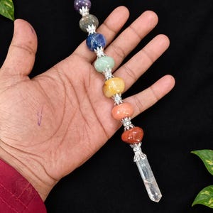 May include: A wand featuring a clear crystal point at one end and a small clear sphere at the other, connected by a series of seven polished, multi-colored gemstone beads separated by silver-toned metal spacers with a floral design.