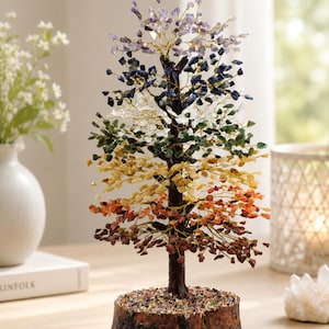 May include: A decorative tree sculpture featuring a dark brown trunk and branches made of thin gold wire. The branches are adorned with small, raw gemstone chips in a gradient of colors, including purple, blue, clear, green, yellow, orange, and red.