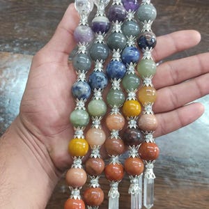 May include: Five vertical wands featuring a series of stacked, multi-coloured spherical gemstone beads separated by silver-toned metal spacers. Each wand is topped with a clear spherical bead and terminates in a clear, pointed crystal point.
