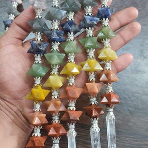 May include: A collection of vertical wands featuring stacked multi-colored star-shaped gemstones separated by silver-toned metal spacers. Each wand is topped with a clear spherical bead and finished at the bottom with a clear crystal point.