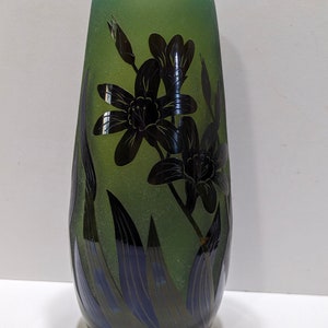 May include: A green glass vase with a frosted finish and black floral design. The vase has a tall, slender shape and a rounded bottom.