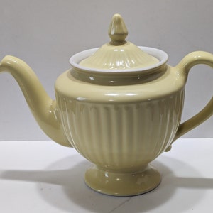 May include: A yellow ceramic teapot with a lid and a fluted design. The teapot has a round body and a spout on one side and a handle on the other.