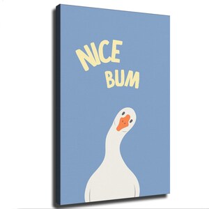 May include: A rectangular canvas wall art piece featuring a light blue background with the text NICE BUM in pale yellow letters. Below the text is a stylized illustration of a white goose with an orange beak, looking forward with its head tilted.