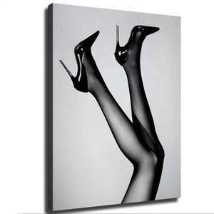 May include: A black and white canvas print featuring a pair of legs wearing sheer black stockings and glossy black high-heeled stiletto shoes. The legs are positioned in the air against a plain, light gray background, creating a high-contrast visual.