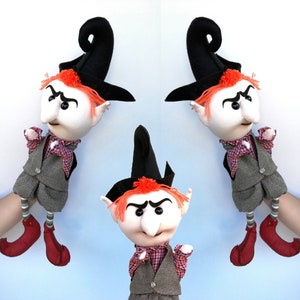 Puede incluir: Tres marionetas de pelo rojo con sombreros negros y chalecos grises. Las marionetas tienen rasgos exagerados, incluyendo narices y cejas grandes. Llevan zapatos rojos y tienen una expresión traviesa.