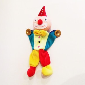 May include: A colorful plush clown doll with a red hat, yellow and red pants, and a blue and green shirt. The clown has a big smile and a red nose.