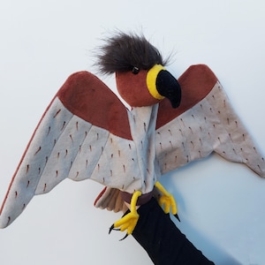 May include: A brown and gray puppet of a hawk with yellow talons and a black beak. The puppet has a brown and gray feathered body and a black head with a brown tuft of fur.