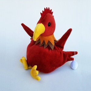 May include: Red plush rooster toy with a yellow beak and brown accents. The rooster is holding a white plush egg.