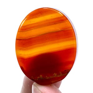 May include: An oval-shaped polished gemstone featuring horizontal bands of colour ranging from deep dark red at the bottom to vibrant orange and bright yellow at the top. The surface is smooth and glossy, displaying natural layered mineral patterns.