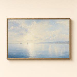 May include: A rectangular landscape painting in a gold frame depicting a calm blue sea under a soft, pale sky with light clouds. Two small sailboats are visible on the horizon, and the water reflects the bright, diffused light from above.