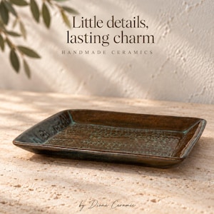 Puede incluir: Una bandeja rectangular de cerámica con un acabado esmaltado en marrón oscuro y verde azulado. El texto "Little details, lasting charm HANDMADE CERAMICS" y "by Dione Ceramic" es visible, con una superficie texturizada.