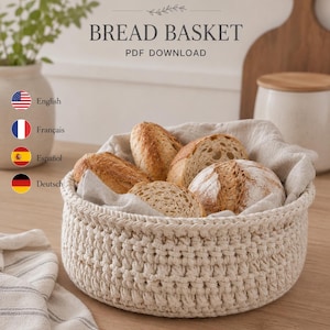 Peut inclure: Un panier à pain rond en crochet blanc cassé doublé d'un tissu beige clair, contenant quatre miches de pain croustillantes. L'image inclut le texte CROCHET PATTERN BREAD BASKET PDF DOWNLOAD et des icônes de drapeaux pour English, Français, Español et Deutsch.