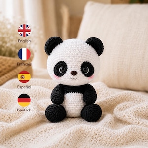 Op de afbeelding: Een gehaakte panda knuffel met een ronde witte kop, zwarte oren en zwarte vlekken rond de ogen. De panda heeft een kleine bruine neus, een geborduurde mond en roze wangen. Het lichaam is wit met zwarte armen en zwarte benen.