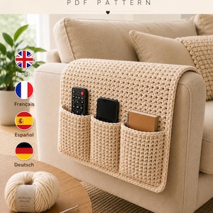 Pode incluir: Um organizador de braço de sofá em crochê bege com três bolsos, contendo um controle remoto, um smartphone e um caderno. O texto CROCHET ARM ORGANIZER PDF PATTERN está visível no topo, acompanhado por um novelo de lã e uma agulha de crochê.
